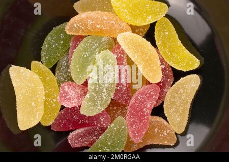 Several sweet marmalade candies on a black ceramic plate, macro, top view. Stock Photo