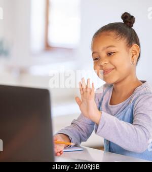 One happy mixed race preschool girl waving to teacher or tutor while having a video call on a laptop for distance learning at home. School kid Stock Photo