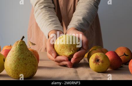 Close-Up of a woman holding a pear in her hands with assorted fruit on the table in front of her Stock Photo