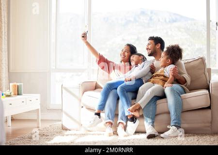 Family selfie of an african american woman, her husband and daughters sitting on the sofa in the living room at home. A young wife taking photos with Stock Photo