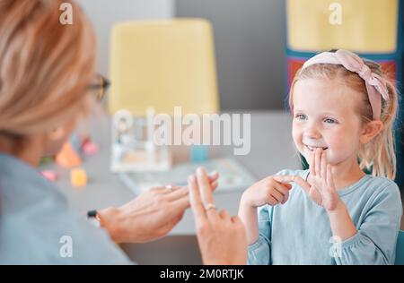 Adorable smiling little caucasian girl standing and using sign language to communicate with child psychologist in a clinic. Mental health professional Stock Photo