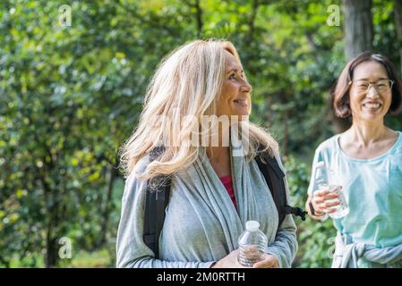 Female senior friends hiking on national park while drinking water Stock Photo