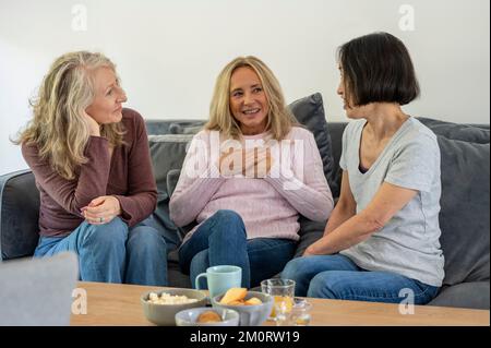 Three senior female friends having a conversation while sitting on sofa at home Stock Photo