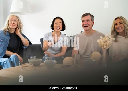 Diverse group of senior friends sitting on sofa watching TV Stock Photo