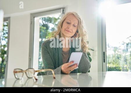 Senior woman using smart phone while sitting at counter Stock Photo