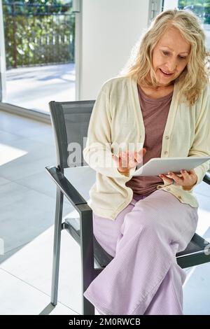 Senior woman using digital tablet while sitting on chair Stock Photo