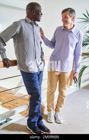 Two diverse middle-aged male friends chatting at home Stock Photo