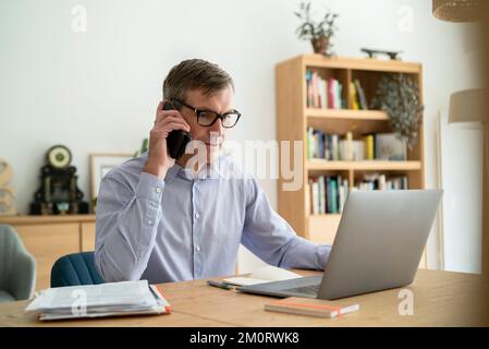 Senior businessman listening to voicemail on smart phone while doing home office Stock Photo