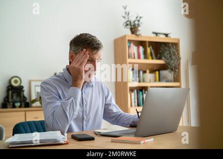 Senior businessman having a headache while using laptop at home Stock Photo