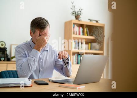 Stressed senior businessman with hand on face doing home office Stock Photo