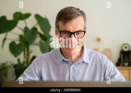 Senior man smiling while using laptop at home Stock Photo