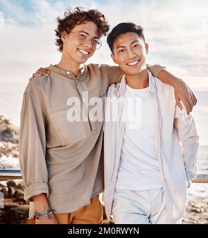 Portrait of two attractive young men standing together on the beach. Asian male and his best friend embracing one another on a day out with friends Stock Photo