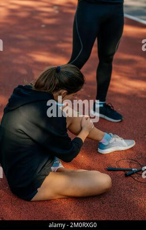 Female athlete feels a pain in her left leg. She was jumping rope for too long. Her boyfriend is standing next to her Stock Photo