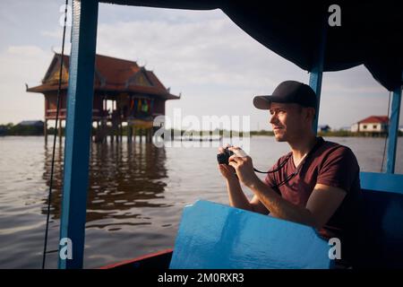 Portrait of tourist with camera on boat floating on lake. Floating village on Tonle Sap Lake near Siem Reap in Cambodia. Stock Photo