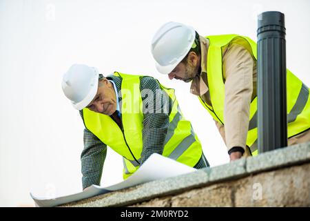Two construction workers are looking at the plans on the paper while having a discussion, close up Stock Photo