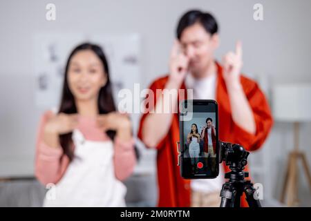 Asian young couple tiktoker creating their dancing video with smartphone camera and tripod. Cute man and woman making a vertical video content to share on social media Stock Photo