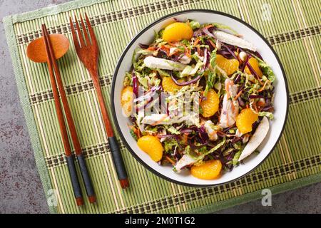 Chinese Chicken Salad with shredded chicken meat, mandarin oranges, crunchy noodles, red cabbage, napa cabbage, carrots, green onions in bowl close-up Stock Photo