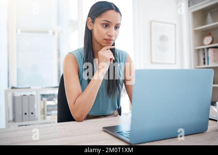 Young mixed race business woman concentrating on work while busy on laptop at her desk. Female entrepreneur sitting at her desk and reading email or Stock Photo