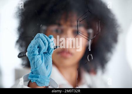 Closeup of the hand of a young mixed female scientist writing and planning on a board wearing goggles and gloves at work. Focused hispanic lab worker Stock Photo
