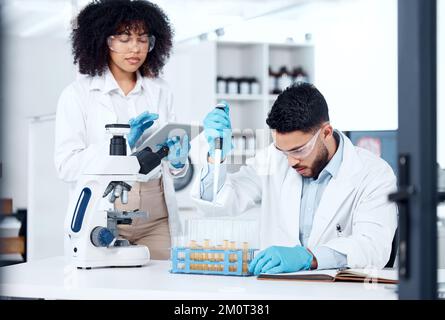 Two mixed race scientists wearing safety equipment while conducting medical research experiments with pipette and test tubes in a lab. Colleagues Stock Photo