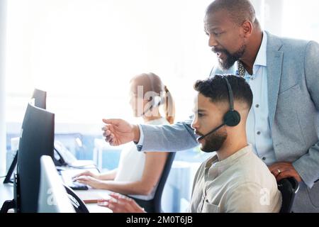 Access the clients account. a mature businessman standing and helping his call centre agents in the office. Stock Photo