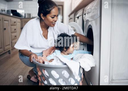She has fun anywhere. a young mother playfully bonding with her baby girl while doing the laundry at home. Stock Photo