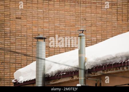 Metal exhaust ventilation pipes on the background of a brick wall. Roof of the house in the snow. Cloudy, cold winter day, soft light. Stock Photo