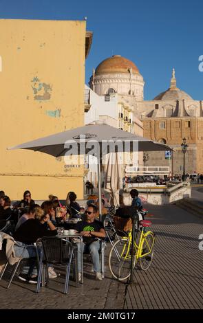 Spain, Andalusia, Cadiz, paseo maritimo, people seated at a sunny caf? terrace in front of the cathedral in the warm light of the sunset facing the sea Stock Photo