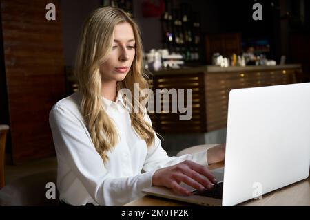 Business woman using computer at workplace in modern cafe. Working for pleasure and success. Office worker doing task remotely. Stock Photo