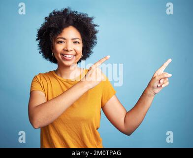 Hey, check this out. an attractive young woman standing alone against a blue background in the studio and pointing at a promotion. Stock Photo