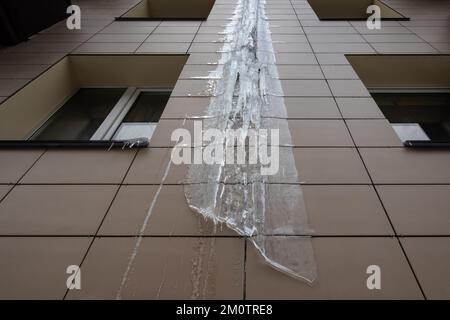 Frozen rain pipe on an apartment building. Ice on the building wall. Stock Photo