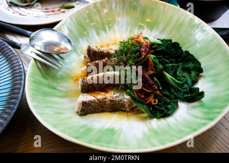 Thai chef cooking food fusion style cuisine roasted grilled fried fillet grouper fish steak with spicy sour sauce and vegetable fruit on ceramic dish Stock Photo