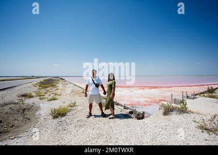 Holding hands couple against red salt lake in Saline Margherita di Savoia of Italy. Stock Photo