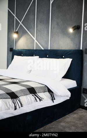 Stylish bedroom interior with big black bed and dark geometric wallpaper on background. Side view of elegant dark colored bed and hanging soft light against gray wall indoors. Concept of interior. Stock Photo