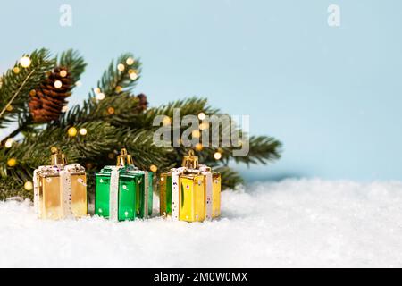 Three Christmas decorations in the form of gold and green gifts near the Christmas tree with twinkling golden lights on a blue background. Merry Chris Stock Photo
