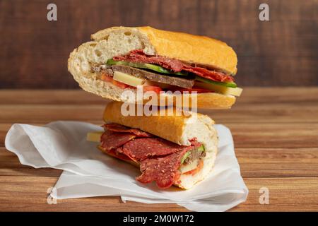 Baguette sandwich. Sandwich with salami, roast beef, cheddar, tomato and cucumber on wooden background Stock Photo