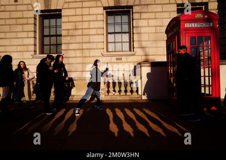 Tourists form a queue to take photographs with a red phone box in Parliament Square, Westminster during sunny weather in London. The Met Office has issued a number of weather warnings for snow and ice for parts of Scotland, Northern Ireland, Wales and the east coast and south-west England over the coming days. Picture date: Thursday December 8, 2022. Stock Photo