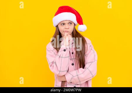 pondering child in santa claus hat on yellow background, party Stock Photo