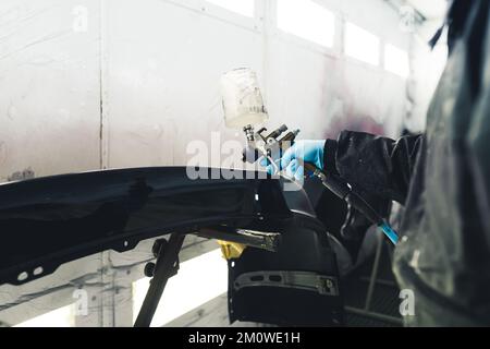 Medium closeup shot of unrecognizable mechanic in protective clothing using paint spray gun on a car fender. Automobile painting and varnishing. High quality photo Stock Photo