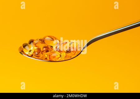Close-up Vitamin D in Omega 3 or fish oil capsules in a spoon on yellow background,Nutritional supplements,vitamin pills, alternative healthy medicine Stock Photo