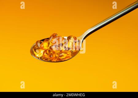 Close-up Vitamin D in Omega 3 or fish oil capsules in a spoon on yellow background,Nutritional supplements,vitamin pills, alternative healthy medicine Stock Photo