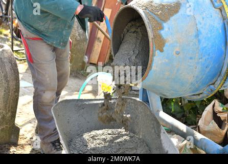 A bricklayer pours concrete from a temperer into a wheelbarrow traditionally in the village Stock Photo