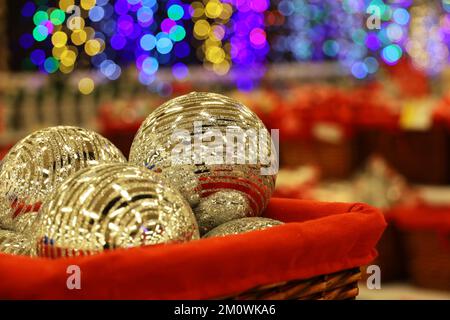 Christmas toys, golden balls in red basket on blurred festive lights background. New Year decorations in a store Stock Photo