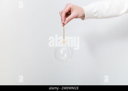 Female hand holding transparent glass Christmas ball on white backdrop. Trendy Christmas background Stock Photo