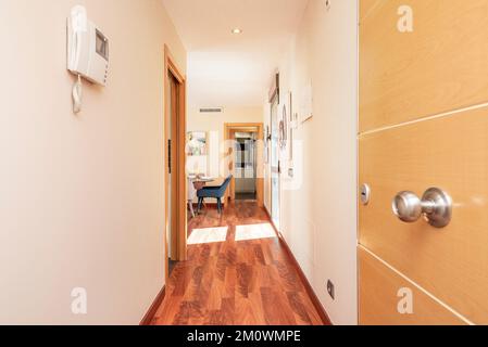 Entrance hall of a house with an armored access door, a corridor that leads to the living room and reddish parquet floors Stock Photo