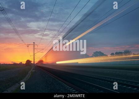 Modern railway at beautiful sunrise. Light trail of train on railroad track. Moving modern intercity passenger train. Stock Photo