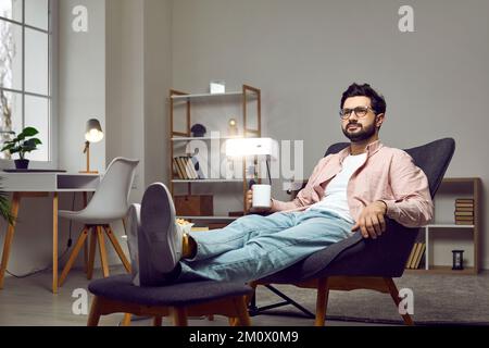 Relaxed man sitting in an armchair at home, using a projector, watching a movie, drinking coffee Stock Photo
