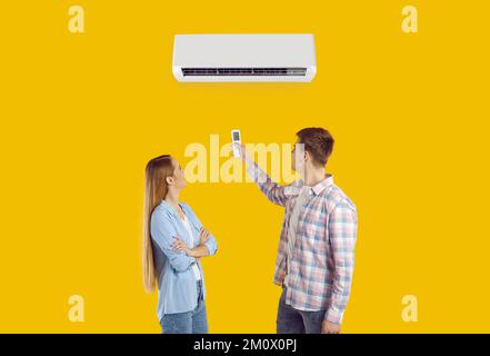 Happy couple use remote to set temperature on air conditioner isolated on yellow background Stock Photo