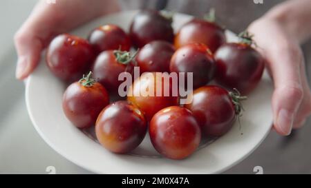 Retail and business, ripe black tomatoes on a plate in the hands of a woman. Stock Photo