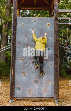 Boy At The Climbing Wall Without A Helmet, Danger At The Climbing Wall. Little Boy Climbing A Rock Wall Indoor Stock Photo